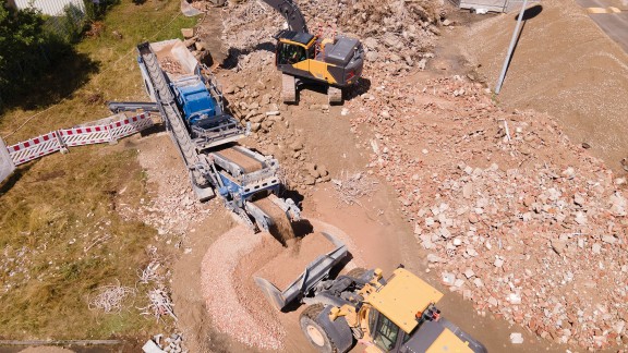 Vista aérea de una trituradora de impacto eléctrica en una obra de demolición, rodeada de escombros.