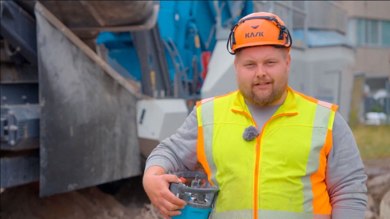 Retrato de un hombre vestido de obra. Lleva en la mano un mando a distancia para la instalación trituradora.