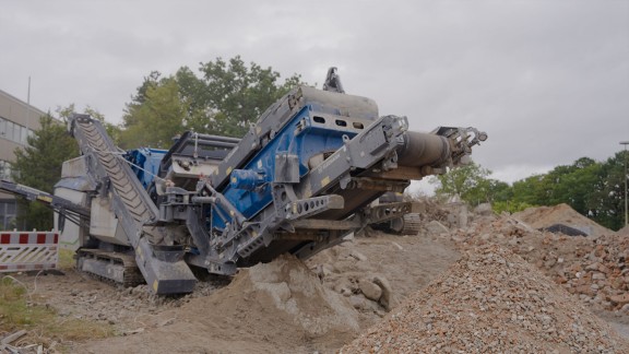 Trituradora de impacto eléctrica en una obra de demolición, rodeada de escombros.