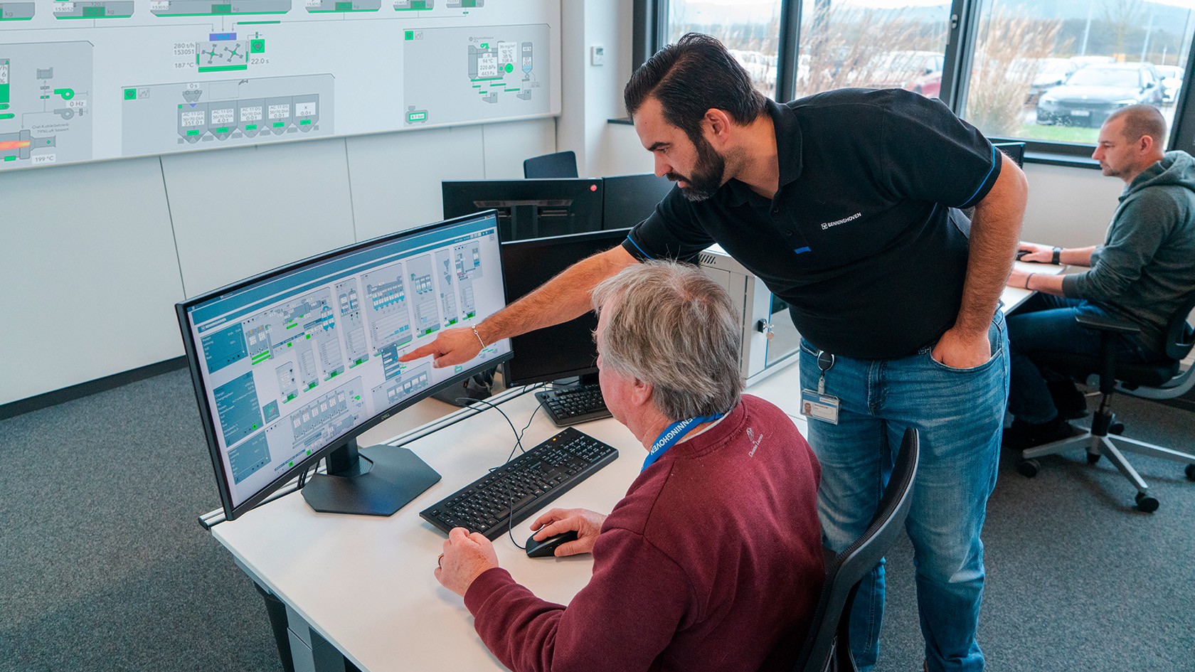 Training session: An operator sits at the control system screen while a trainer stands behind, pointing something out on the display. 