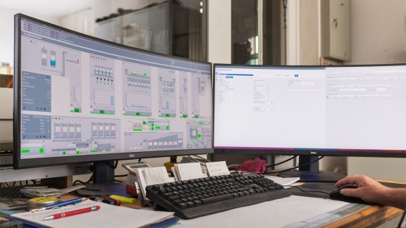 Two computer monitors showing graphical control system functions.