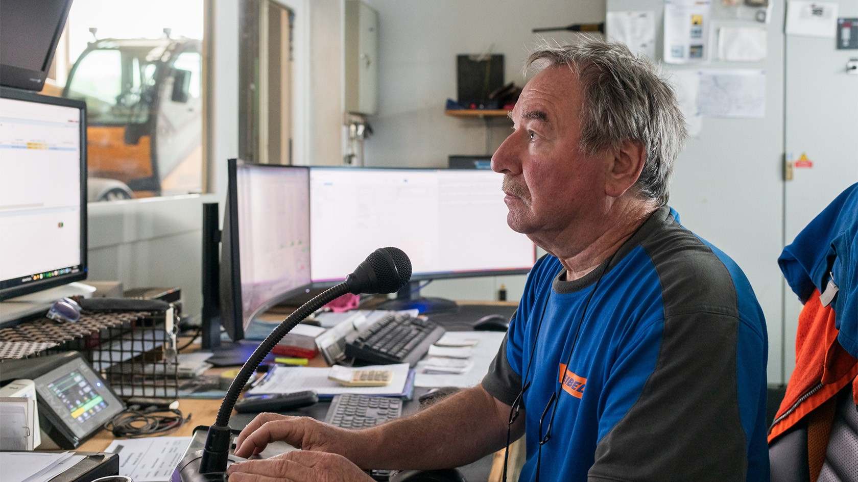 The mixing foreman sitting at a desk, with a microphone in the foreground and computer screens in the background