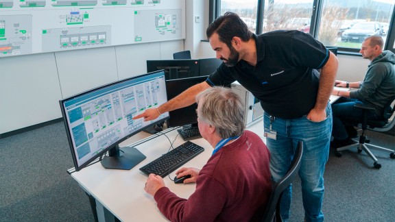 Training situation: Mixing foreman sitting at a computer, course instructor leaning over him and pointing at the screen.