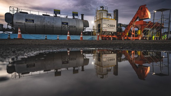 La centrale d’enrobage se reflète dans une flaque.
